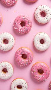 Assorted pink and white frosted donuts with colorful sprinkles scattered across a pink background for an iPhone wallpaper.