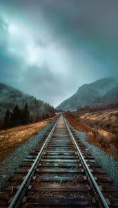 An iPhone wallpaper depicting a moody scene with train tracks extending into the distance through a misty, mountainous landscape.